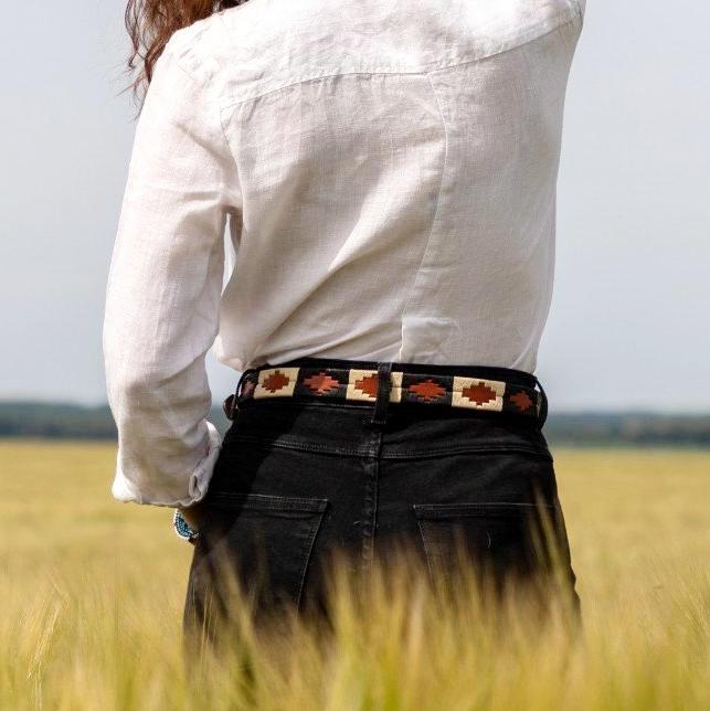 Femme de dos portant un look noir et blanc avec une ceinture de polo argentine dans les passants d'un jean noir. Femme seen from the back wearing black and white outfit with a polo argentinian belt in the loops of a pair of jeans.