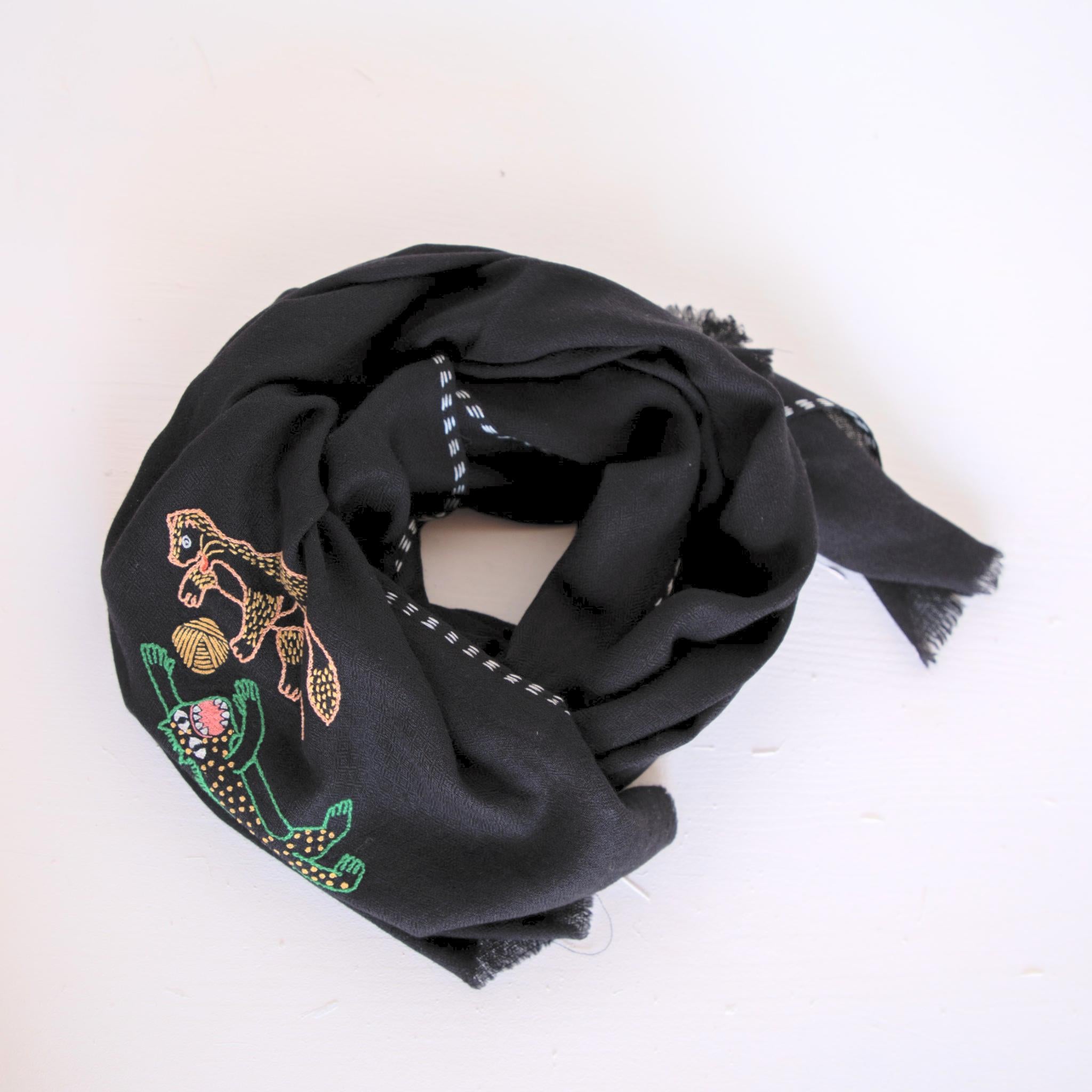 Femme dans un champ de blé portant une étole en pashmina noire brodée réalisée en collaboration avec Laïte Works. Woman in a wheat field wearing a black embroidered pashmina stole, in collaboration with Laïte Works.