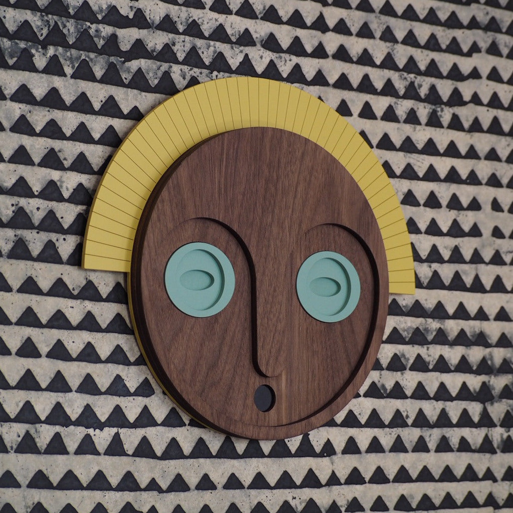 Décoration murale en bois, représentant un masque aux yeux jades et couronne jaune, en édition limitée par UMASQU. Wooden wall decoration, evoking an african mask with jade eyes and yellow crown made by UMASQU in limited edition.