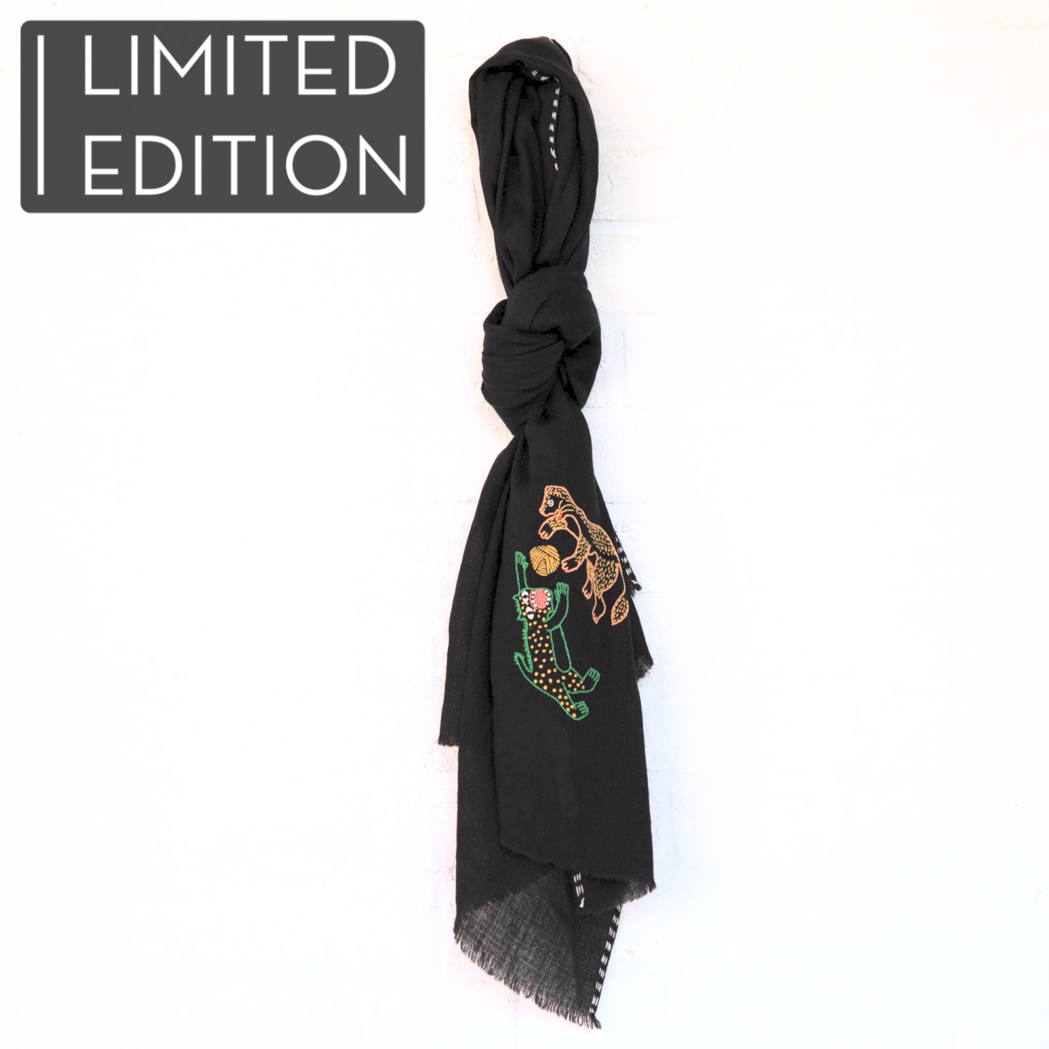 Femme dans un champ de blé portant une étole en pashmina noire brodée réalisée en collaboration avec Laïte Works. Woman in a wheat field wearing a black embroidered pashmina stole, in collaboration with Laïte Works.