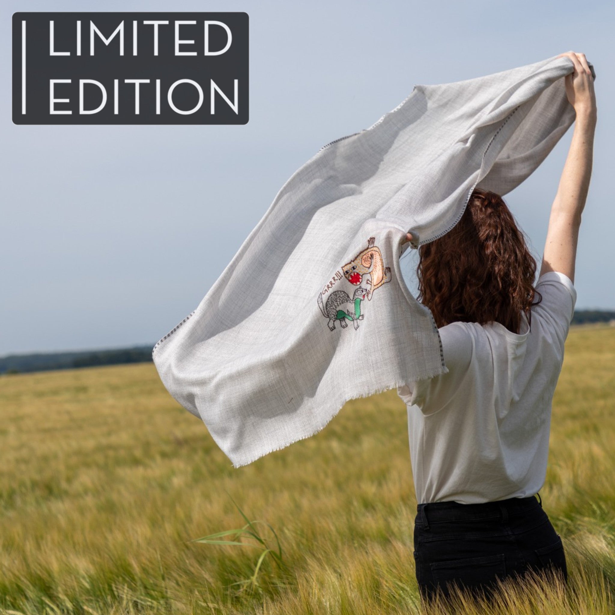 Femme dans un champ de blé portant un pashmina gris clair brodé réalisé en collaboration avec Laïte Works. Woman in a wheat field wearing a grey embroidered pashmina, in collaboration with Laïte Works.