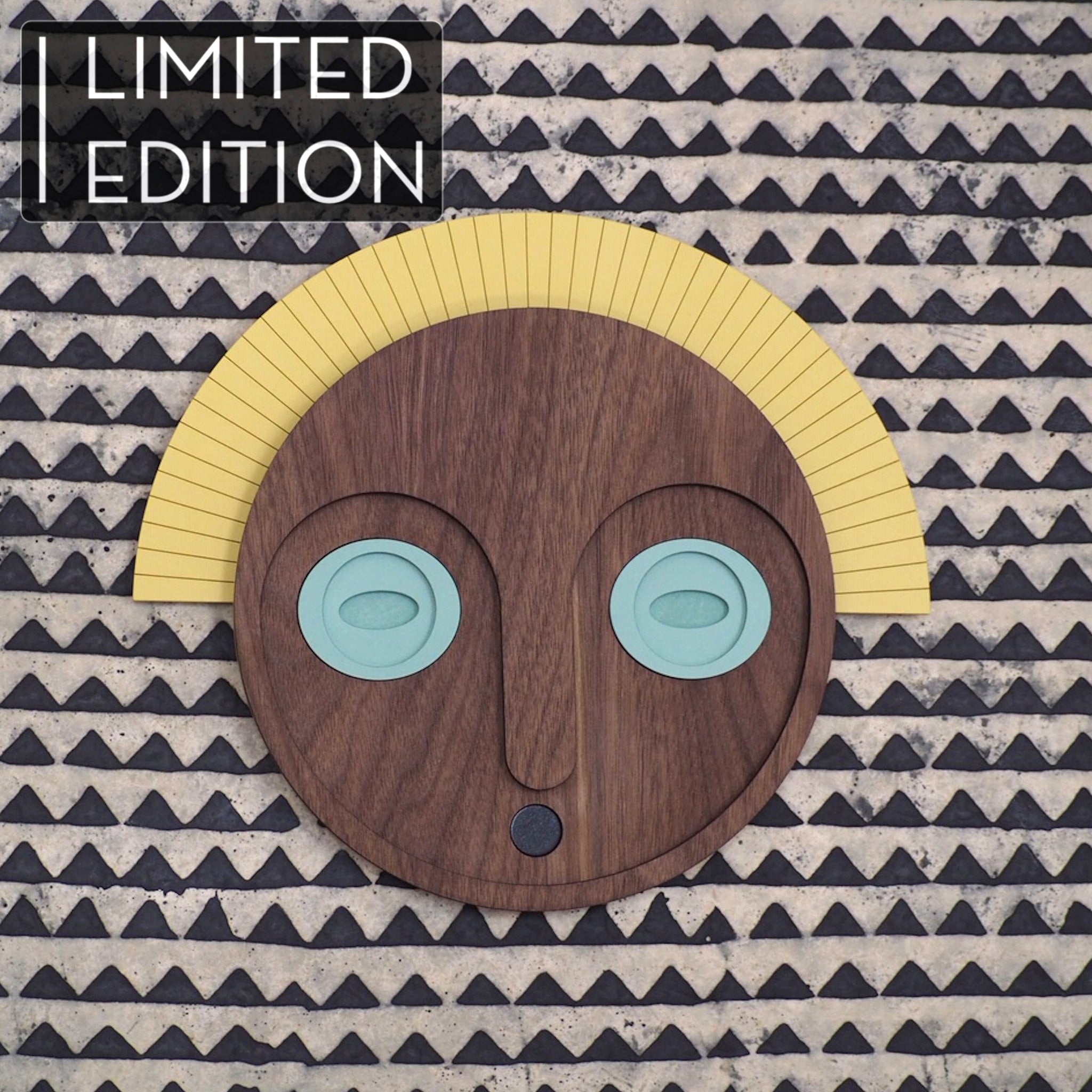 Décoration murale en bois, représentant un masque aux yeux jades et couronne jaune, en édition limitée par UMASQU. Wooden wall decoration, evoking an african mask with jade eyes and yellow crown made by UMASQU in limited edition.